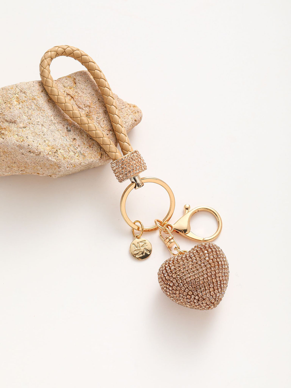 Portachiavi composto da un anello dorato su cui si agganciano due componenti: un cuore tridimensionale completamente ricoperto di strass colorato e un manico intrecciato in pelle sintetica.
