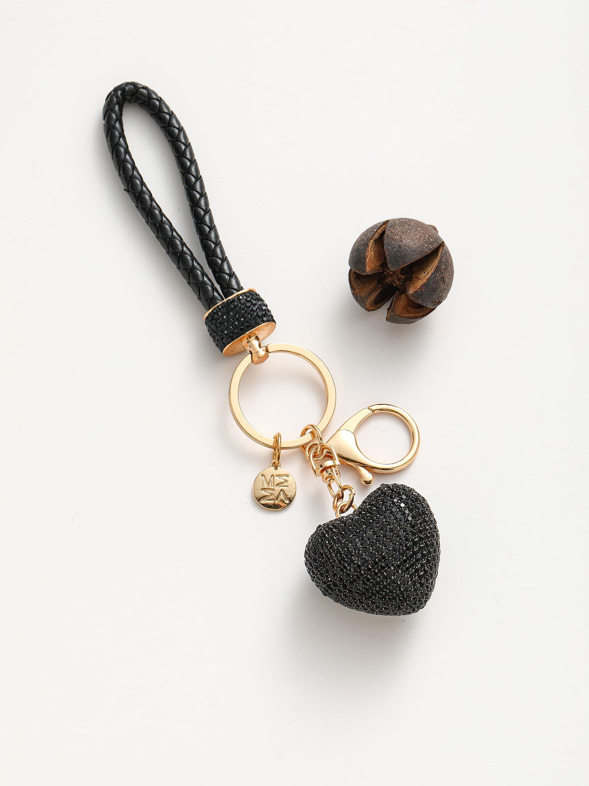 Portachiavi composto da un anello dorato su cui si agganciano due componenti: un cuore tridimensionale completamente ricoperto di strass colorato e un manico intrecciato in pelle sintetica.